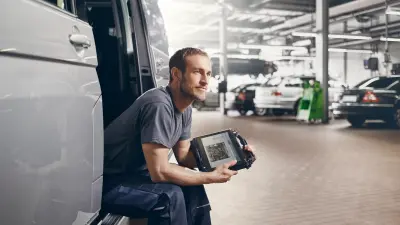 Workshop operator is sitting in an open van with a tablet in his hands.